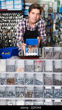 Homme debout près du comptoir et détails de vente pour la plomberie dans l'atelier de quincaillerie Banque D'Images