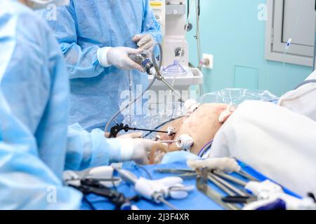 Une équipe de chirurgiens intervient sur un patient par des perforations dans la cavité abdominale. Mise au point sélective. Les médecins portant des uniformes bleus stériles et des gants en latex blanc travaillent sur un patient sur la table d'opération Banque D'Images