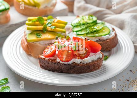 Pain grillé au seigle et au blé avec féta, tomates cerises, avocat et concombre. Des collations saines. Crostini avec feta. Banque D'Images