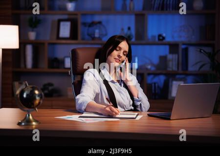 Jeune femme d'affaires souriante, belle femme d'affaires parlant au téléphone au bureau. Portrait d'affaires d'une femme attrayante assise sur le lieu de travail. Conversation Banque D'Images