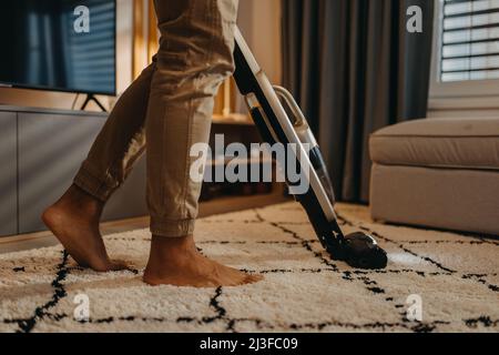 Section basse d'homme à accrocher un tapis avec aspirateur dans le salon Banque D'Images