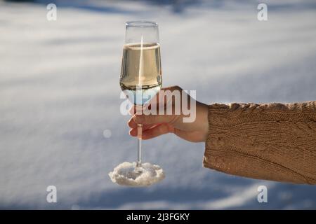 La main d'une femme dans un chandail chaud tient un verre de champagne sur un fond enneigé. Vacances d'hiver Banque D'Images