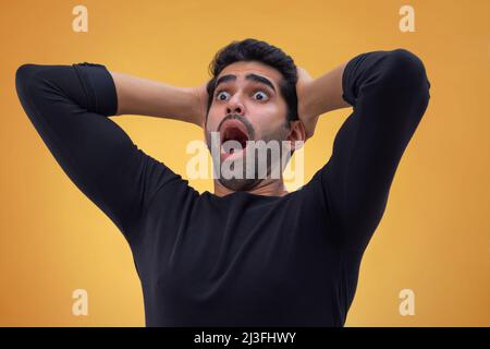 Portrait d'un jeune homme étourdi avec des yeux larges, des mains sur sa tête et regardant ailleurs avec la bouche ouverte Banque D'Images