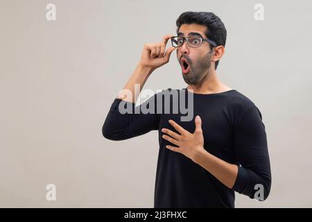 Portrait d'un jeune homme étourdi regardant ailleurs avec la bouche ouverte, les yeux larges et les mains sur sa poitrine Banque D'Images