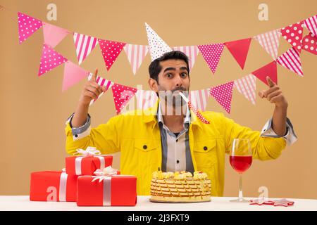 Joyeux jeune homme soufflant corne de fête à son anniversaire Banque D'Images