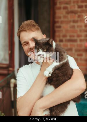 Homme tenant le chat entre les mains. Gris britannique Cat Homme avec chat souriant. Effet pluie Banque D'Images