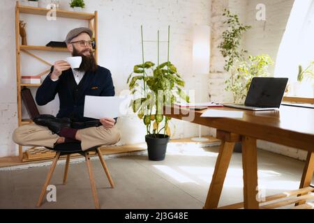 Jeune barbu, employé de bureau s'amusant, faisant du yoga sur une table en bois dans un bureau moderne au travail avec des gadgets. Concept d'entreprise, sain Banque D'Images