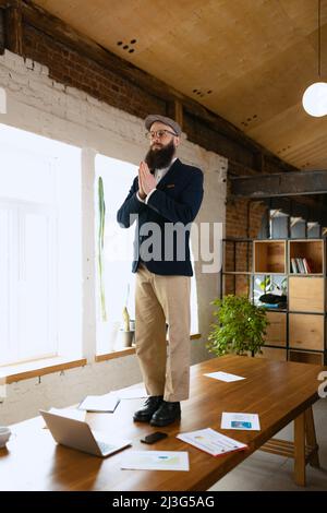 Jeune barbu, employé de bureau s'amusant, faisant du yoga sur une table en bois dans un bureau moderne au travail avec des gadgets. Concept d'entreprise, sain Banque D'Images