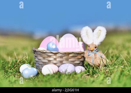 Panier de Pâques avec œufs peints et poussin avec oreilles de lapin sur la prairie Banque D'Images