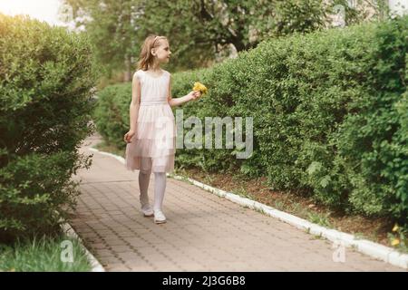 petite fille souriante avec un bouquet de pissenlits qui marchent le long de la rue Banque D'Images