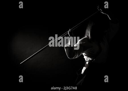 Une fille en hakama noir debout dans la posture de combat avec une épée en bois bokken sur fond sombre. Faible profondeur de champ. Noir et blanc Banque D'Images