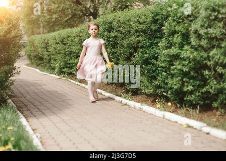 petite fille avec un bouquet de pissenlits marchant sur le trottoir. Banque D'Images