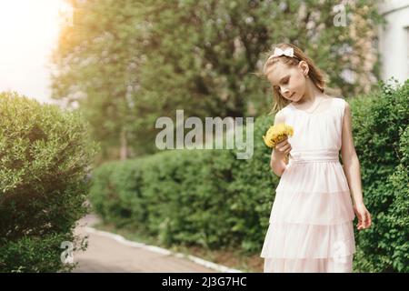 petite fille souriante avec un bouquet de pissenlits qui marchent le long de la rue Banque D'Images