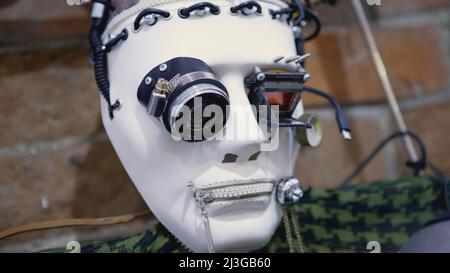 Masque robot de style cyber-punk. ART. Masque en plastique blanc avec caméras dans les yeux. La face du robot dans les fils noirs est clouée à un mur de brique Banque D'Images