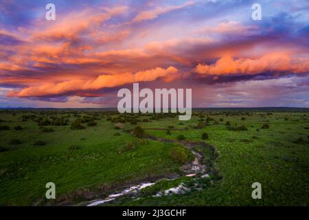 Image aérienne d'un magnifique coucher de soleil tandis que la pluie tombe à l'horizon sous un paysage dynamique de nuages rose et orange, avec une rivière au premier plan. Banque D'Images