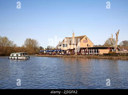 Le Ferry Inn près de la rivière Bure sur les Norfolk Broads un jour de printemps tôt avec un croiseur passant à Horning, Norfolk, Angleterre, Royaume-Uni. Banque D'Images