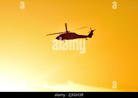 Silhouette de l'hélicoptère militaire Sikorsky Black Hawk UH-60 en vol et survolant l'océan Pacifique au coucher du soleil doré, San Diego, Californie, États-Unis Banque D'Images