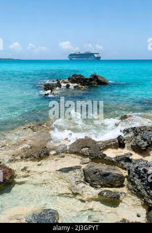 La vue d'une vague de lavage de rochers et d'un bateau de croisière dérivant en arrière-plan (Bahamas). Banque D'Images