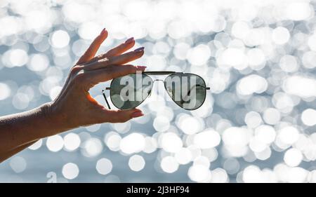 Lunettes de soleil dans une main de femme sur fond flou avec des réflexions de bokeh Banque D'Images