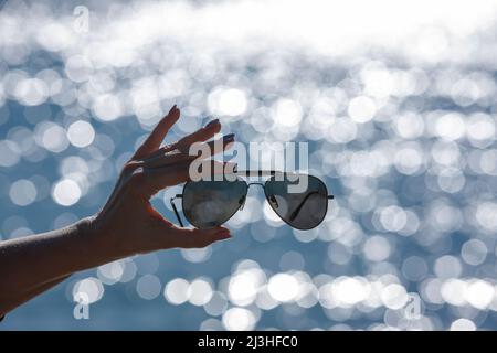 Lunettes de soleil dans une main de femme sur fond flou avec des réflexions de bokeh Banque D'Images