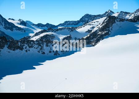 Deux grimpeurs dans les hautes montagnes enneigées d'hiver sur le Lüsenser Ferner par une journée ensoleillée. Glacier et pics rocheux sous ciel bleu. Alpes de Stubai, Tyrol, Autriche, Europe Banque D'Images