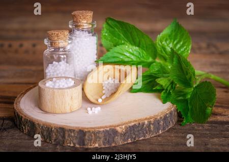 Flacons médicaux en verre sur table en bois, remplis de globulis. Décoration aux feuilles vertes fraîches. Homéopathie conzept. Banque D'Images