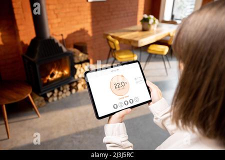 Femme contrôlant la température de la maison avec une tablette numérique à distance Banque D'Images