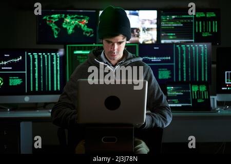 Prise de vue avant de à Hacker en train de pénétrer les serveurs de données d'entreprise depuis son hideout souterrain. L'endroit a une atmosphère sombre, plusieurs écrans Banque D'Images