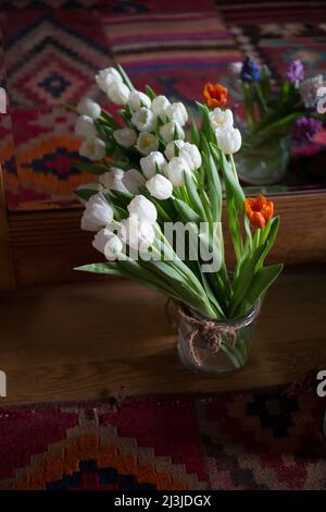 Bouquet de tulipes blanches avec une tulipe orange simple devant un meuble en miroir Banque D'Images