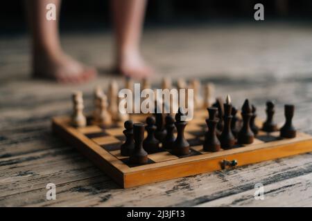 Gros plan sélectif de jambes pieds nus femme debout près de chessboard sur parquet vintage en bois dans la pièce sombre, pensant au mouvement d'échecs. Banque D'Images