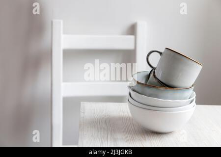 Une pyramide de bols blancs, assiettes et tasses de différentes tailles et couleurs sur une table beige dans la cuisine.Style scandinave.Place pour votre texte.Copier Banque D'Images