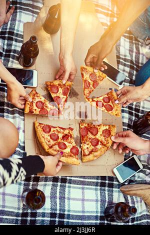 Bonne nourriture, bons amis, des moments glorieux. Photo d'un groupe d'amis qui mangent de la pizza pendant un pique-nique. Banque D'Images