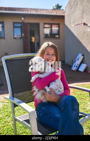 Doublez la coupe ici. Portrait d'une petite fille heureuse assise sur une chaise et tenant son chien à l'extérieur. Banque D'Images