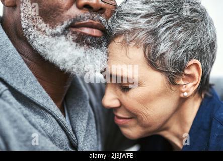 Son endroit le plus sûr est dans ses bras. Photo courte d'un couple senior affectueux qui se détend sur le canapé à la maison. Banque D'Images