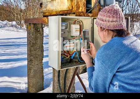 Lecture à partir d'un compteur d'électricité en utilisant Handy par femme dans la campagne en plein air. Banque D'Images