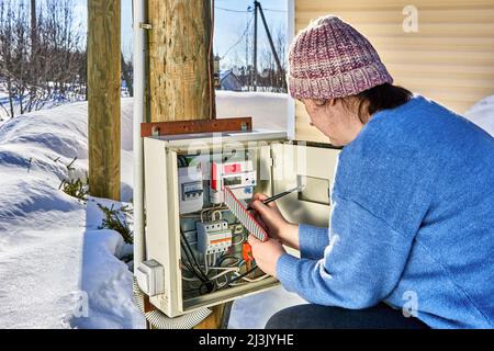 Lecture de compteurs électriques par une femme à l'extérieur du village en hiver. Banque D'Images