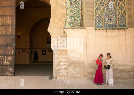 Deux jeunes femmes se tiennent le long d'un mur près d'une entrée au Maroc; Meknes, au Maroc Banque D'Images