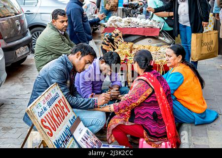 Femme qui reçoit des tatouages au henné (Mehndi Art) sur les mains tout en étant assise dans une rue de la ville à côté d'un vendeur de bijoux; Amritsar, Punjab, Inde Banque D'Images