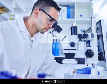 Exécution de quelques tests. Plan rogné d'un beau jeune scientifique travaillant avec un microscope dans son laboratoire. Banque D'Images
