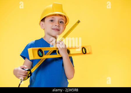 Le préchooleur tient un niveau de construction entre ses mains, rêve de devenir un constructeur. Banque D'Images