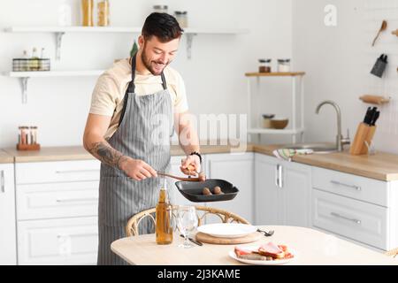 Jeune barbu mettant des saucisses frites sur une assiette dans la cuisine Banque D'Images