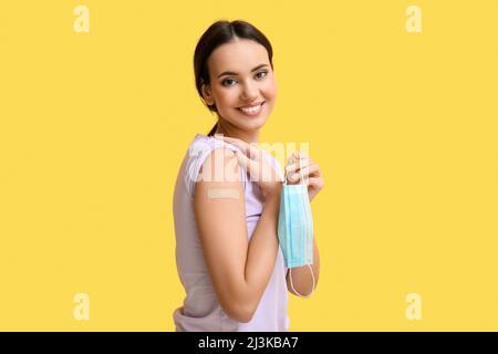 Jeune femme avec patch médical appliqué et masque sur fond jaune Banque D'Images