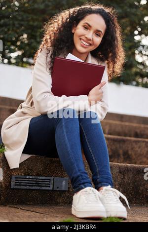 Prêt pour ma prochaine classe. Portrait d'une jeune étudiante d'université attrayante assise à l'extérieur du campus pendant sa pause. Banque D'Images