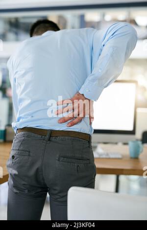 HES a été assis trop longtemps. Vue arrière d'un jeune homme d'affaires tenant le dos tout en se tenant à son bureau. Banque D'Images