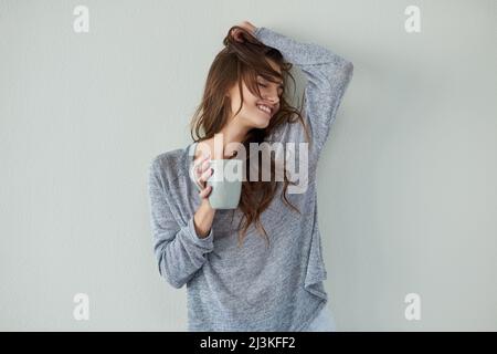 Je suis d'humeur insouciante aujourd'hui. Photo studio d'une jeune femme attrayante avec son bras relevé tout en buvant du café sur fond blanc. Banque D'Images