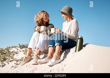 Faire de la plage leur propre café personnel. Prise de vue en longueur de deux belles femmes matures qui apprécient un café tout en étant assis sur la plage. Banque D'Images