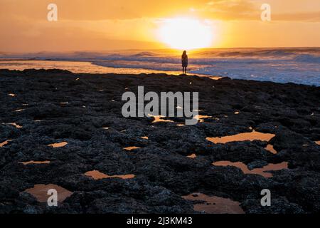 Une jeune femme regarde les vagues et le coucher du soleil de Rocky Point. Banque D'Images