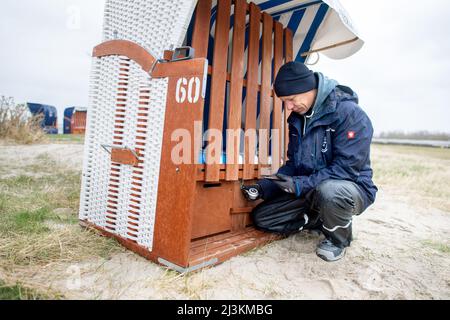 Hooksiel, Allemagne. 05th avril 2022. Jakob Rybarczyk, représentant du service à la clientèle de la société BeachBuddy, monte une serrure numérique sur une chaise de plage. À l'aide d'une application, les visiteurs peuvent réserver et ouvrir les chaises de plage avec leur smartphone. Les préparatifs pour le début de la saison sont en cours sur la côte de la mer du Nord en Basse-Saxe. Credit: Hauke-Christian Dittrich/dpa/Alay Live News Banque D'Images