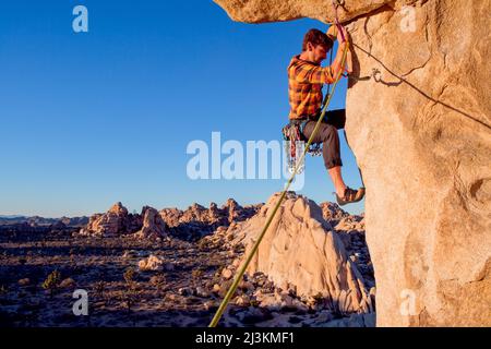 Un grimpeur s'attaque à un surplomb au-dessus de la Vallée Cachée dans Joshua Tree National Park au coucher du soleil. Banque D'Images