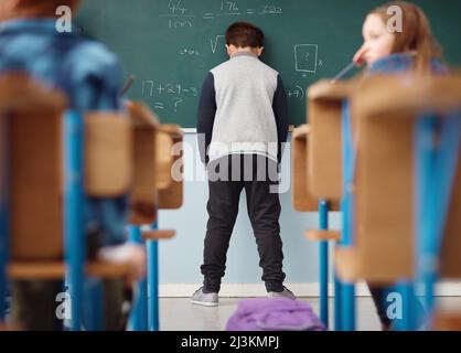 Lutte à l'école. Vue arrière d'un garçon de l'école primaire penché avec sa tête sur le tableau noir en classe. Banque D'Images